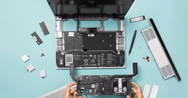 A close-up of a modular Framework Laptop 16 motherboard showing exposed RAM slots on a wooden desk with tools.
